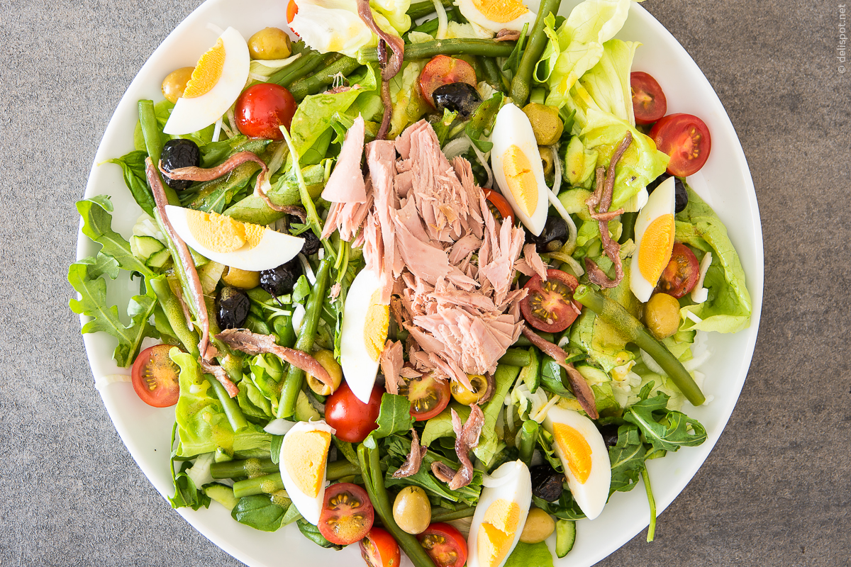 Salade niçoise aus Kopfsalat, Bohnen, Oliven, Tomaten, Eiern, Thunfisch und Sardellen