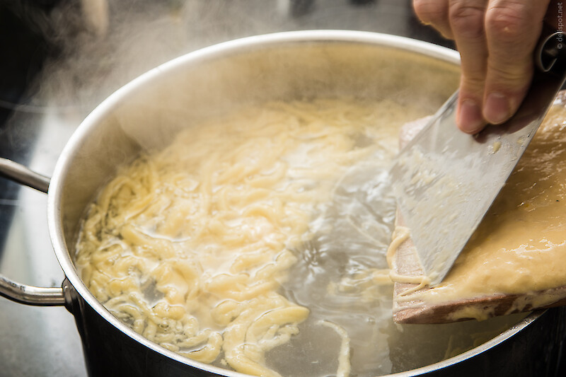 Spätzle werden mit Spätzlesschaber vom Spätzlesbrett in kochendes Salzwasser geschabt