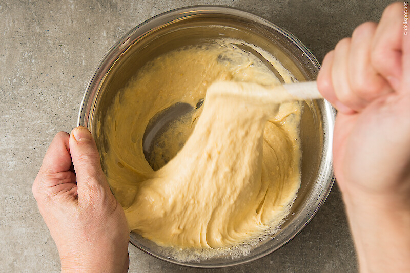 Spätzleteig wird mit einem gelochten Holzlöffel geschlagen