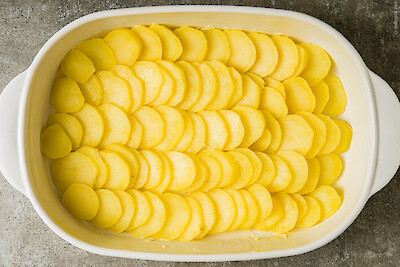 Munster chaud – knapp gegarte Kartoffelscheiben werden in gebutterte Form geschichtet