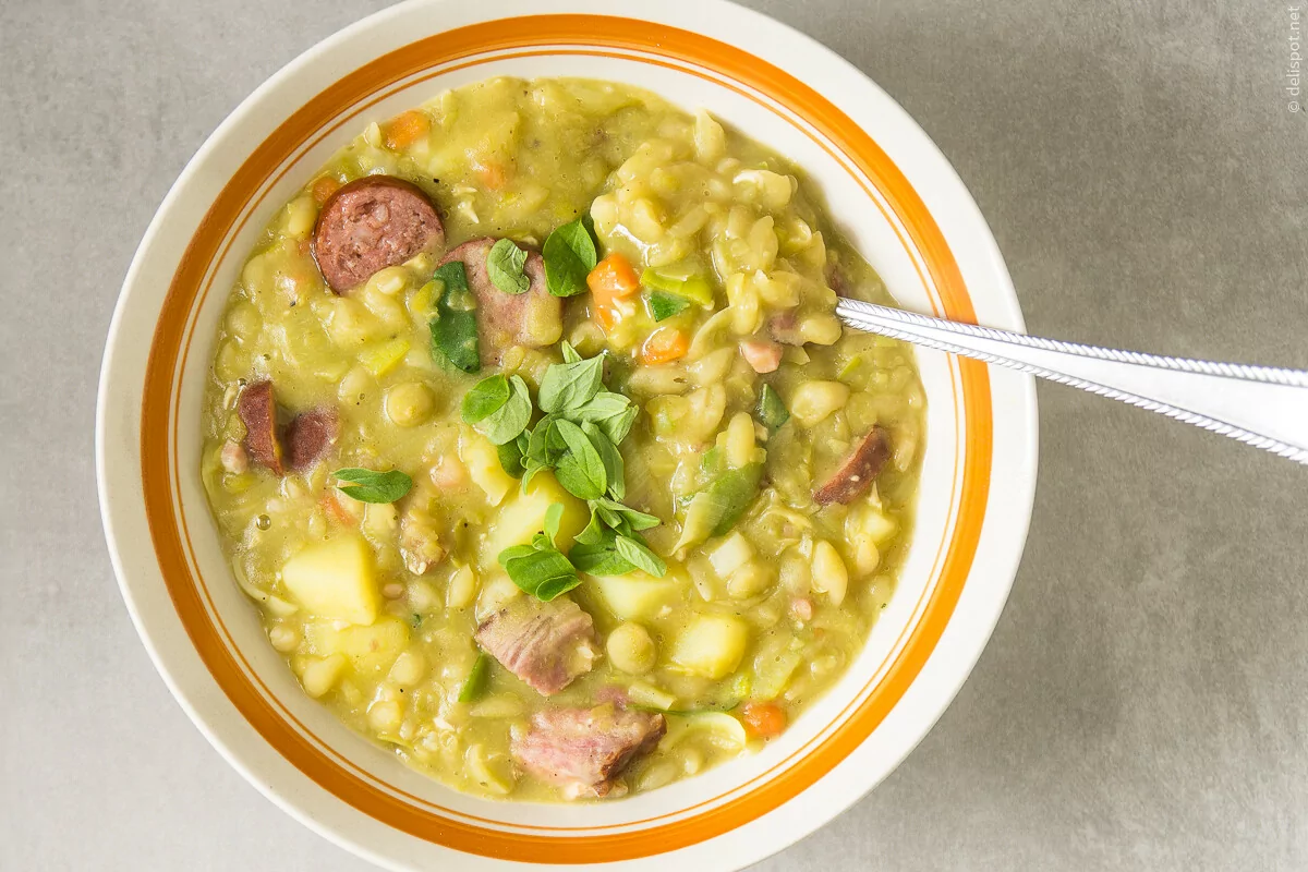 Eine Schale Erbsensuppe mit Einlage aus Gemüse, Kasslernacken und Wurst, bestreut mit frischen Majoranblättchen