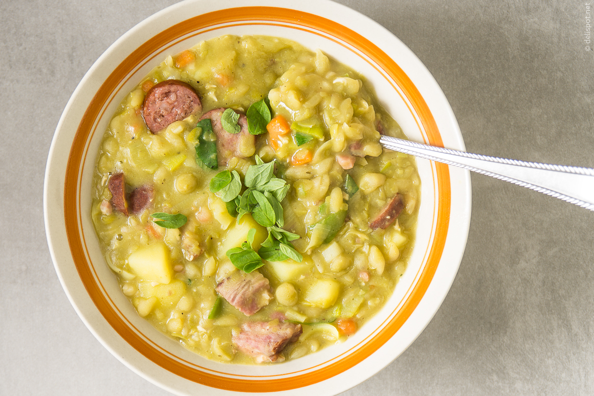 Eine Schale Erbsensuppe mit Einlage aus Gemüse, Kasslernacken und Wurst, bestreut mit frischen Majoranblättchen