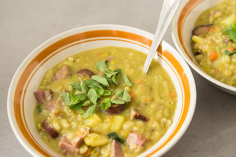 Zwei Schalen Erbsensuppe mit Einlage aus Gemüse, Kasslernacken und Wurst, Garnitur von Majoranblättchen