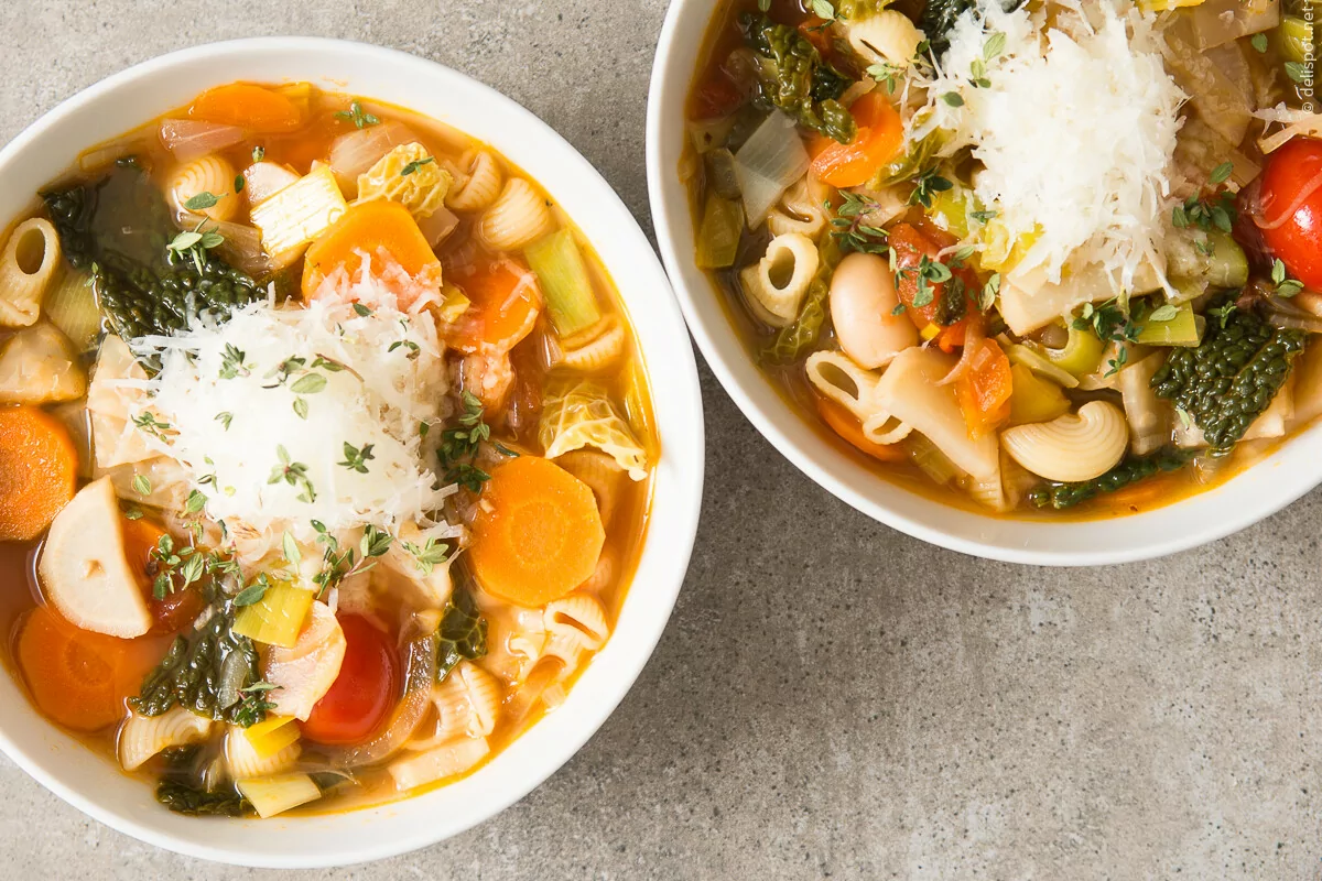 Minestrone, Gemüsesuppe, angerichtet in zwei Schalen, mit Käse und Thymian bestreut