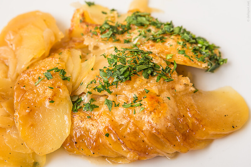 Fertige Bäckerinkartoffeln, auf Teller angerichtet, sie haben Farbe von der Brühe aufgenommen, die sie fast, aber nicht vollständig aufgesogen haben