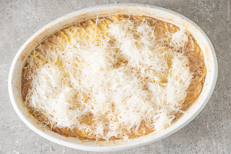 Fast fertig gebackene Bäckerinkartoffeln in einer Auflaufform werden mit einer Schicht Parmesan bedeckt