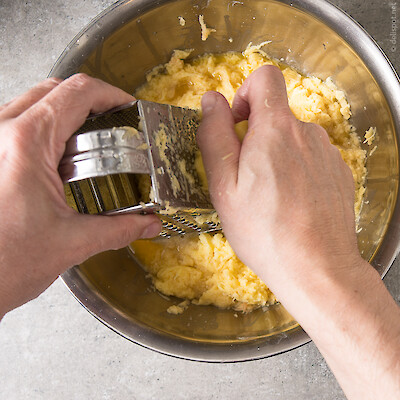 Kartoffeln werden mit Vierkantreibe  in Edelstahlschüssel gerieben, um  Kartoffelpuffer herzustellen