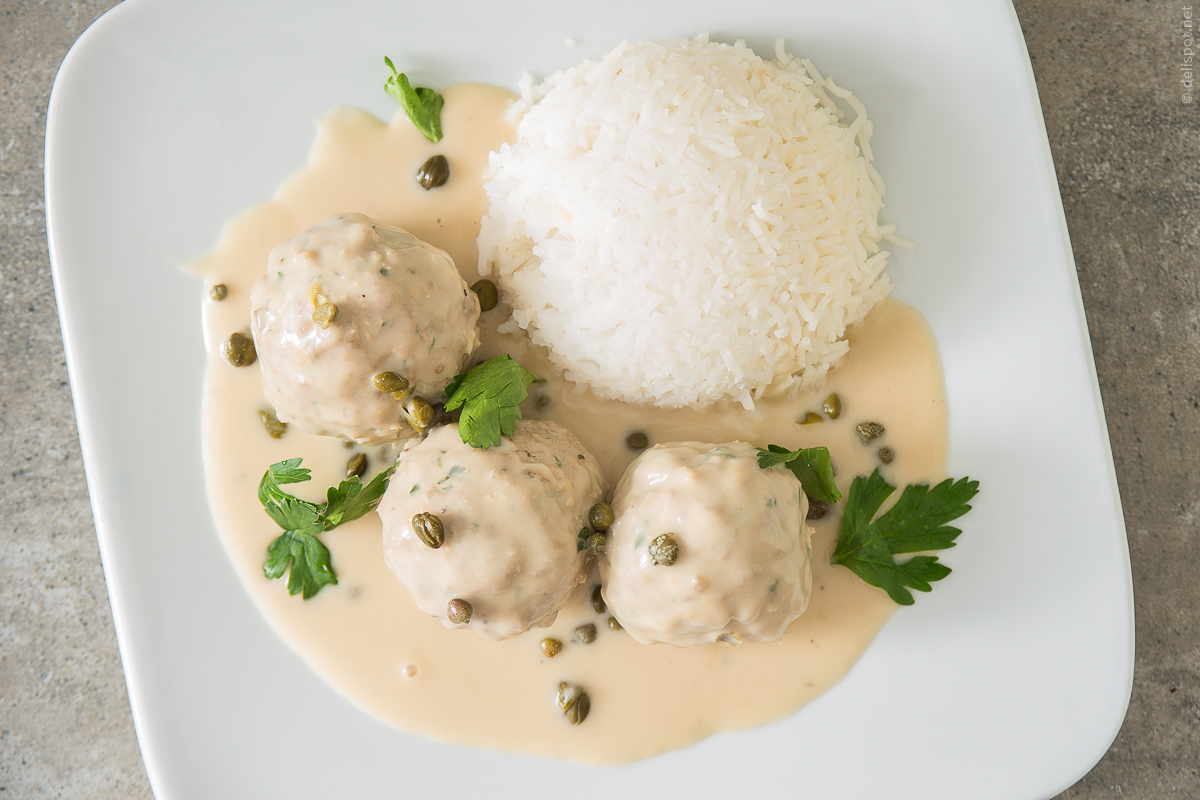 Drei Königsberger Klopse, mit Kapernsauce und Reis auf Teller angerichtet und mit Petersilienblättern garniert